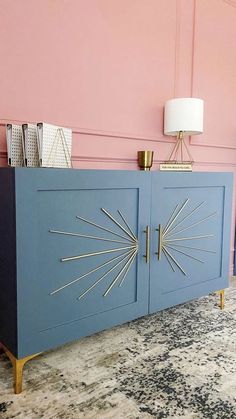 a blue cabinet with gold accents in a pink walled room, next to a lamp