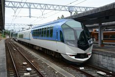 a blue and white train traveling down tracks next to a loading platform at a station