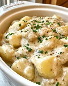 a white bowl filled with potatoes covered in gravy and garnished with chives