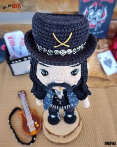 a crocheted doll wearing a hat and holding a guitar sits on a table