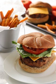 a hamburger with lettuce, tomato and cheese is on a plate next to french fries