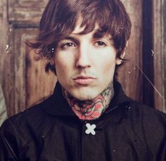 a man with tattoos on his neck standing in front of a wooden wall