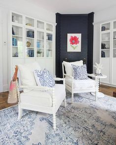 a living room with two white chairs and a blue rug on the floor in front of bookshelves