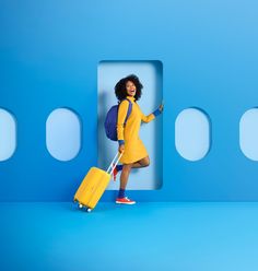 a woman in a yellow dress is holding a blue suitcase and posing for the camera