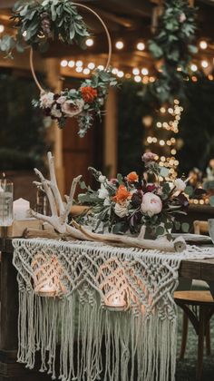 a table with candles and flowers on it in front of some string lights hanging from the ceiling