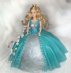 a barbie doll wearing a blue dress and tiara on top of a silver cake