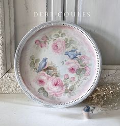 a plate with pink roses and blue birds painted on it sitting in front of a window