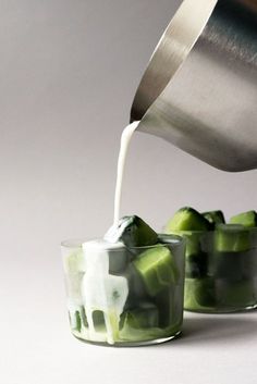 a person pouring something into small glasses filled with cucumber and ice cubes