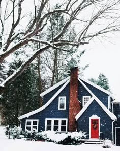 a blue house covered in snow with red door and windows on the front side, surrounded by trees