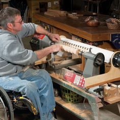 a man sitting in a wheel chair working on a piece of wood with a machine behind him