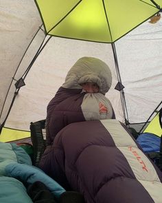 a man in a sleeping bag inside of a tent with an umbrella over his head