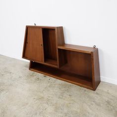 a wooden shelf sitting on top of a floor next to a white wall in an empty room