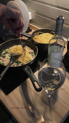 someone is cooking pasta in a skillet on the stove with a bottle of wine