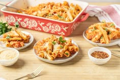 several plates of pasta and seasoning on a wooden table next to a red casserole dish