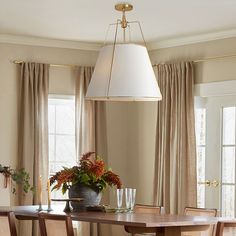 a dining room table with four chairs and a potted plant on the table in front of two windows