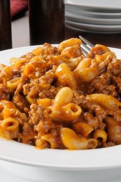 a white plate topped with pasta covered in meat and sauce on top of a table