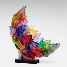 a multicolored glass sculpture sitting on top of a wooden base in front of a white background