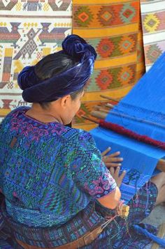 a woman sitting on the ground weaving fabric