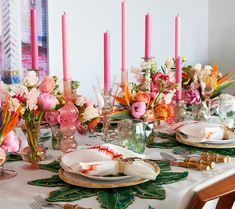 the table is set with pink and orange flowers in vases, candles, and plates