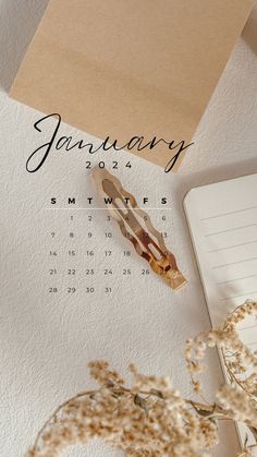 a calendar, pen and dried flowers on top of a white desk with a notepad