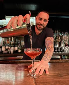 a man pouring a drink into a glass at a bar with lots of bottles behind him