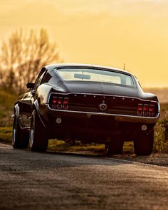 an old muscle car is parked on the side of the road in front of some bushes