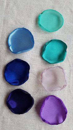 six different shades of blue, purple, and green on a white tablecloth with some fabric