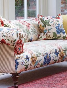 a floral couch sitting on top of a red rug in front of a large window