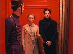 two men and a woman standing in front of a red door, looking at each other