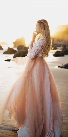 a woman standing on top of a beach next to the ocean wearing a pink dress