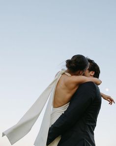 a bride and groom embracing each other in front of the sky with their arms around each other