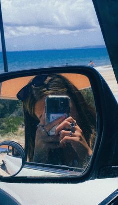 a woman taking a selfie in the side view mirror of a car near the beach