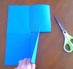 someone is cutting out some blue paper with scissors on a wooden table next to a pair of scissors