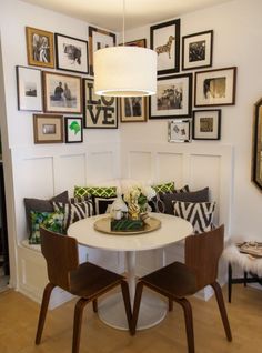 a white table with two chairs and pictures on the wall behind it in a living room