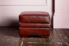 a brown leather footstool sitting on top of a wooden floor next to a pink wall