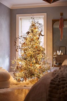 a decorated christmas tree in front of a window next to a bed with pillows and blankets