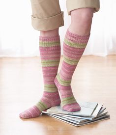 a person wearing pink and green socks standing on top of stack of magazines in front of a window