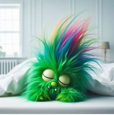 a green monster with multicolored hair laying on a bed