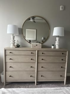 a dresser with two lamps and a round mirror