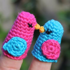 two small crocheted birds sitting on top of each other's fingernails