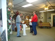 two men and a woman standing in a room with christmas decorations on the wall behind them