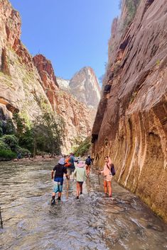 several people are wading through the water in a narrow canyon with mountains in the background