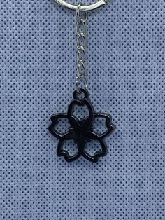 a black flower shaped keychain hanging from a metal ring on a blue background