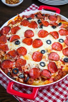 a pepperoni pizza with olives and cheese in a red pan on a checkered tablecloth