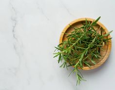 a wooden bowl filled with green herbs on top of a white counter