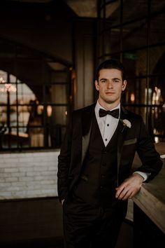 a man in a tuxedo standing next to a wall and looking at the camera