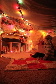 a person sitting on the floor in front of a book shelf with christmas lights hanging from it