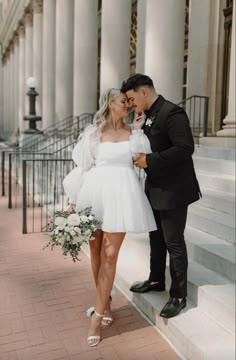 a bride and groom are standing on the steps in front of a building with columns