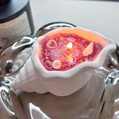 a white bowl filled with a red candle on top of a metal tray next to a bottle