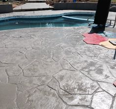 an outdoor patio area with concrete floors and chairs around the pool in the back yard